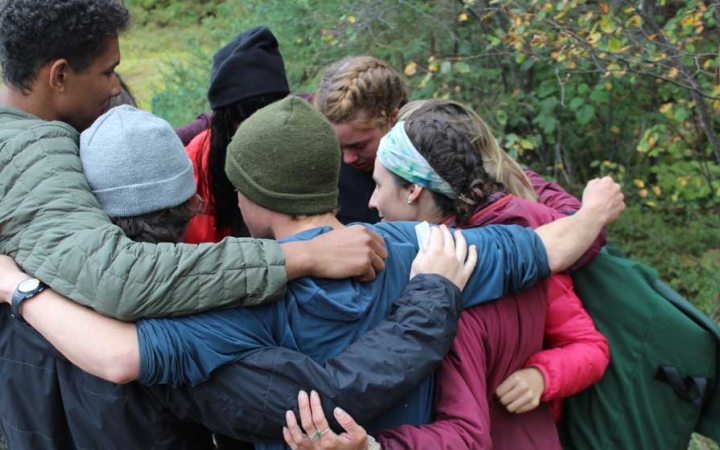 A group of students huddle in a circle with their arms around one another. 